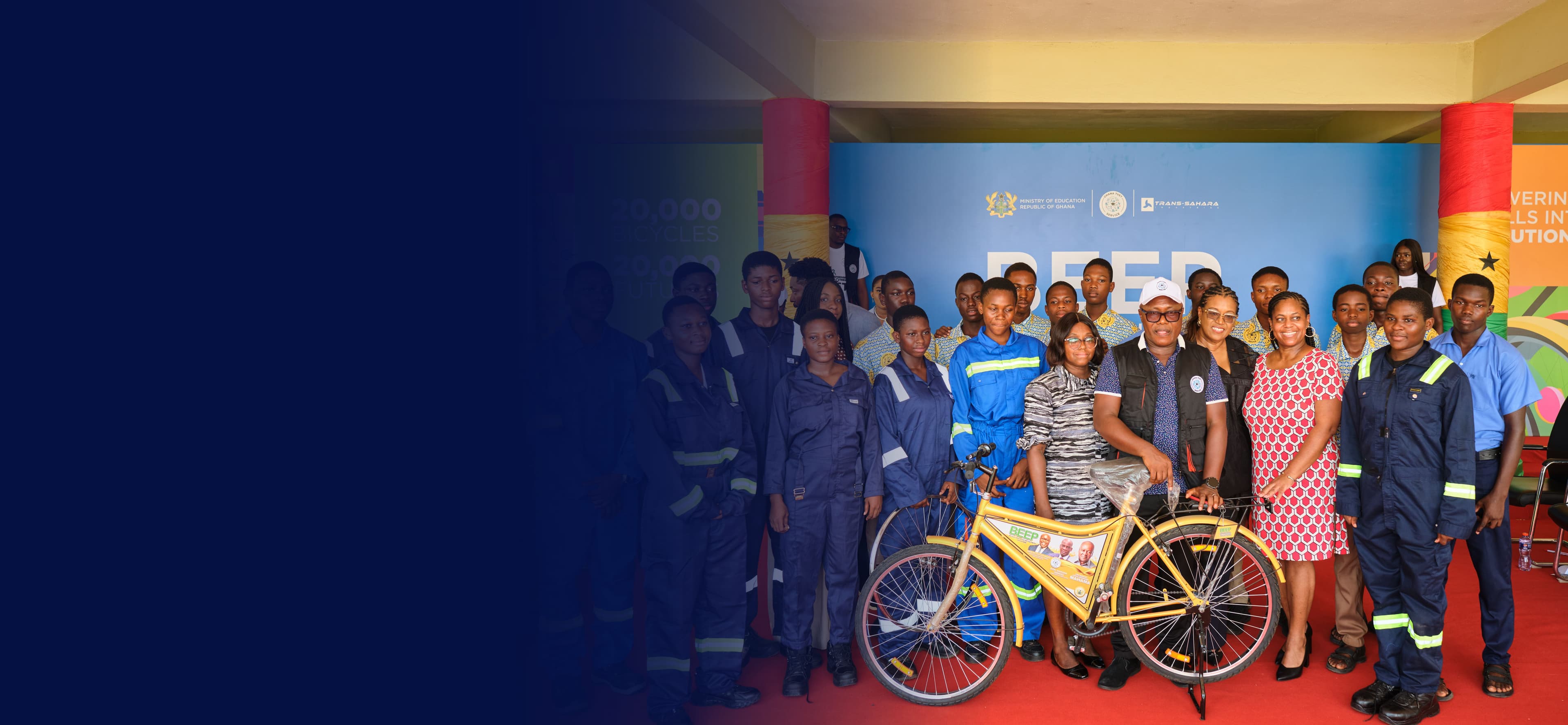 Ghana TVET Service trainees in workshop coveralls with Ministry of Education and Trans-Sahara Industries officials at the BEEP programme launch, beside a yellow BEEP bicycle
